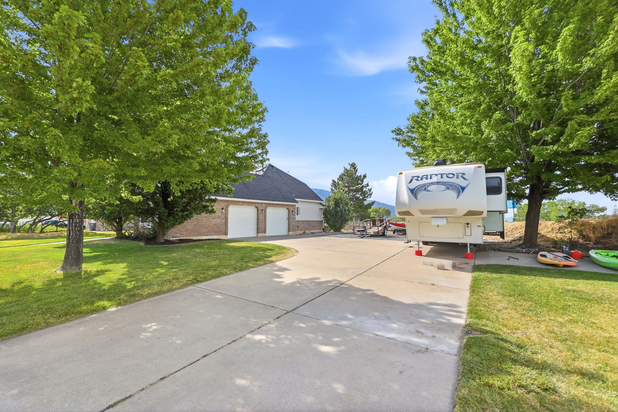 Spacious concrete driveway featuring a three-car garage with white doors, expansive lawn areas, and mature trees providing shade
