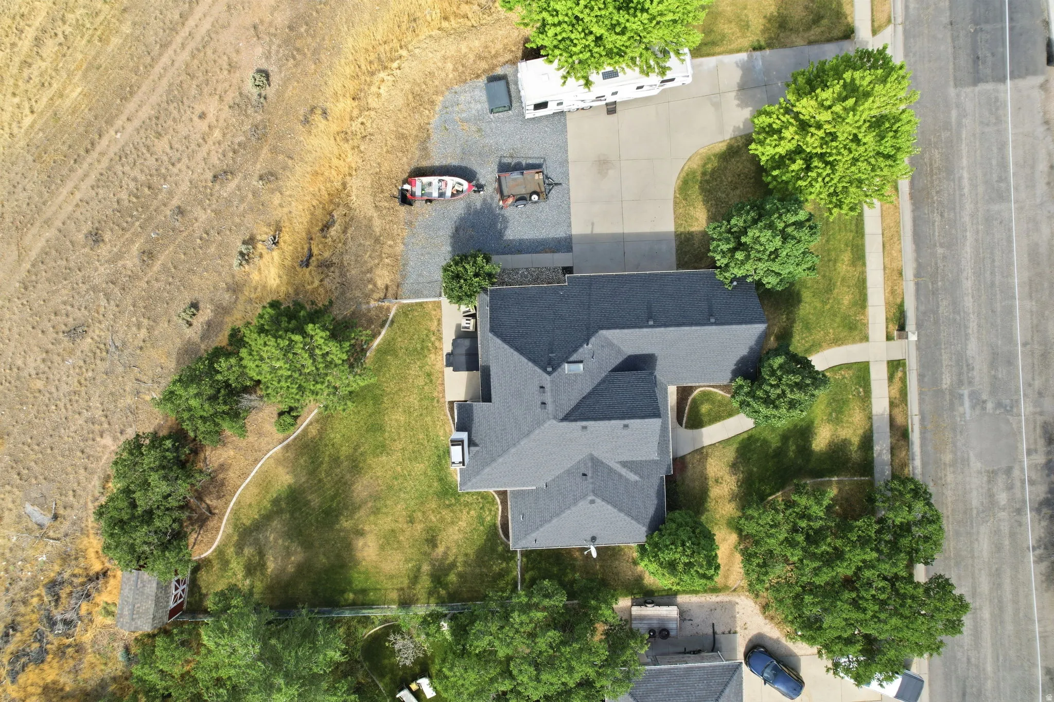 Spacious property featuring a large asphalt driveway, expansive lawn areas, and mature trees providing shade