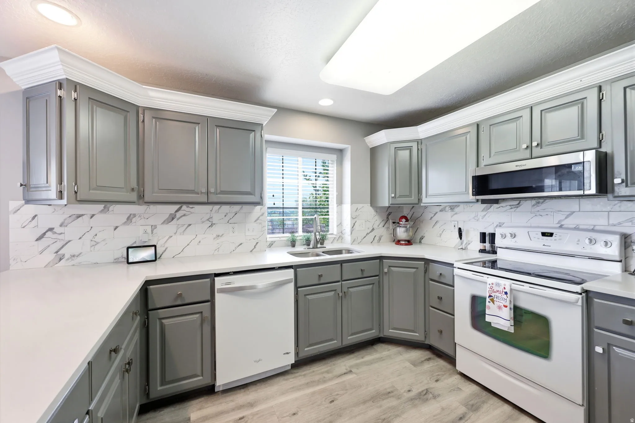 Modern kitchen featuring light gray cabinetry, white countertops, and a white subway tile backsplash with gray veining