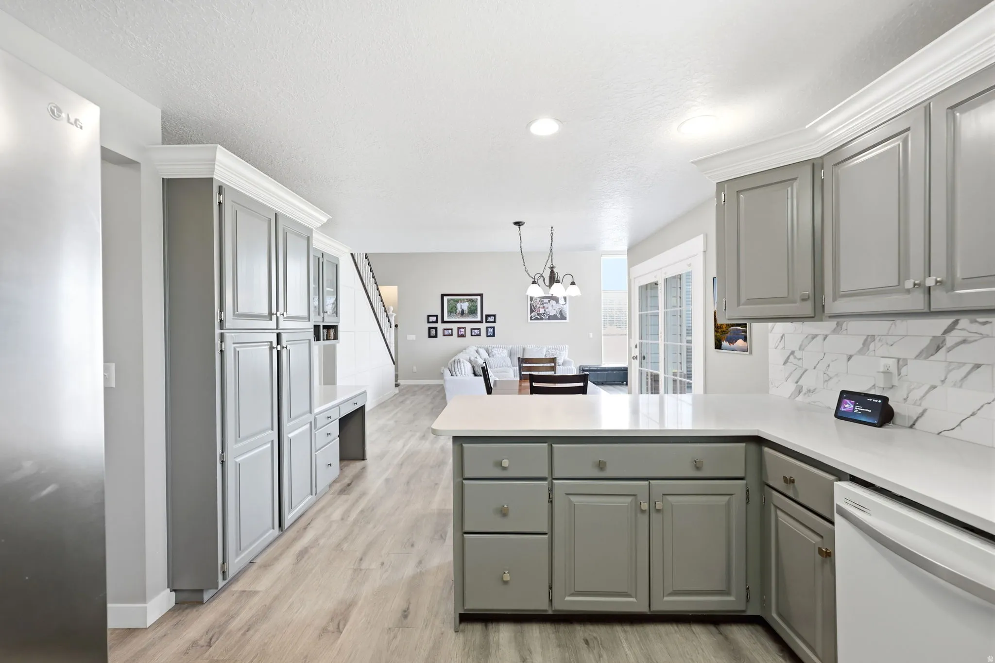 Contemporary kitchen featuring light gray cabinetry, light wood-finish flooring, white countertops, and a white marble-patterned backsplash