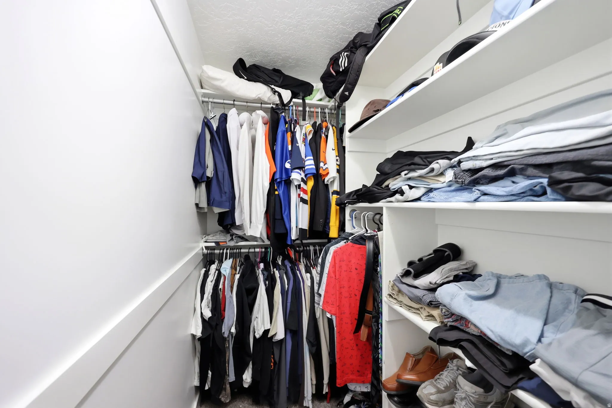 Walk-in closet featuring built-in shelving, multiple hanging rods, white walls, and a textured ceiling