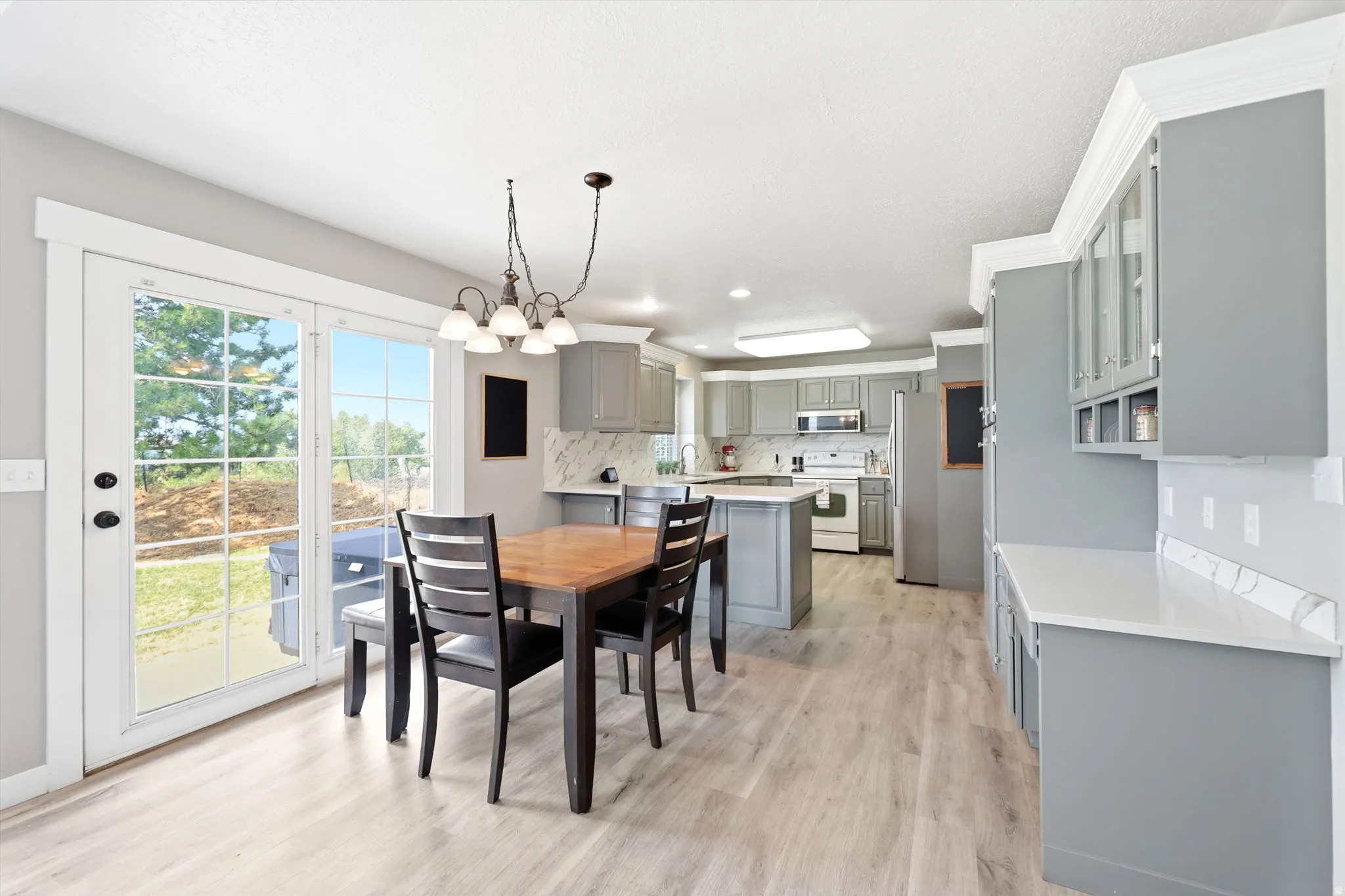 Open-concept kitchen and dining area featuring light wood-finish flooring, a kitchen island with seating, grey cabinetry, white countertops, and a white tile backsplash