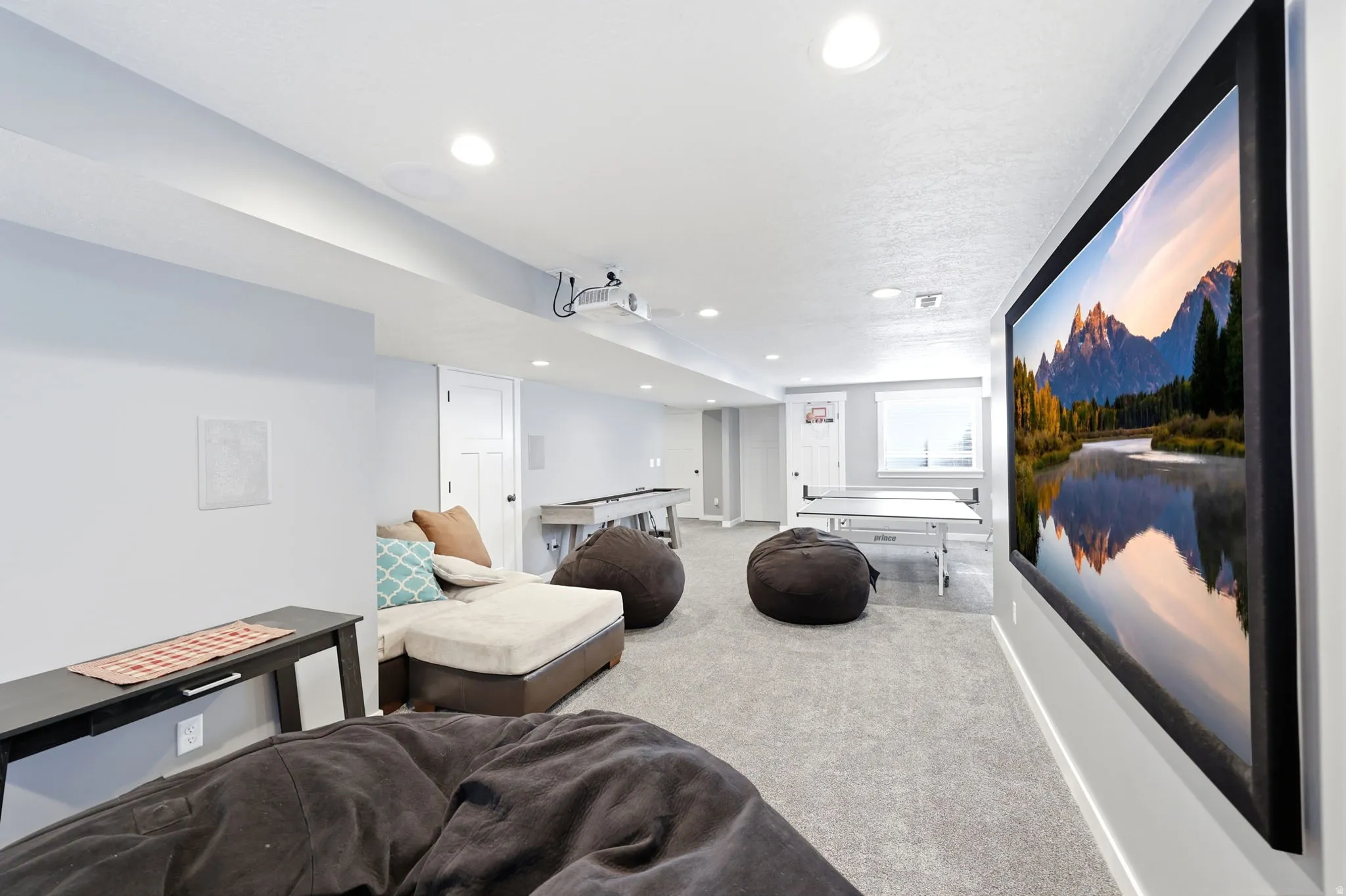 Expansive recreation room featuring a large wall-mounted screen, recessed lighting, and light gray carpeting