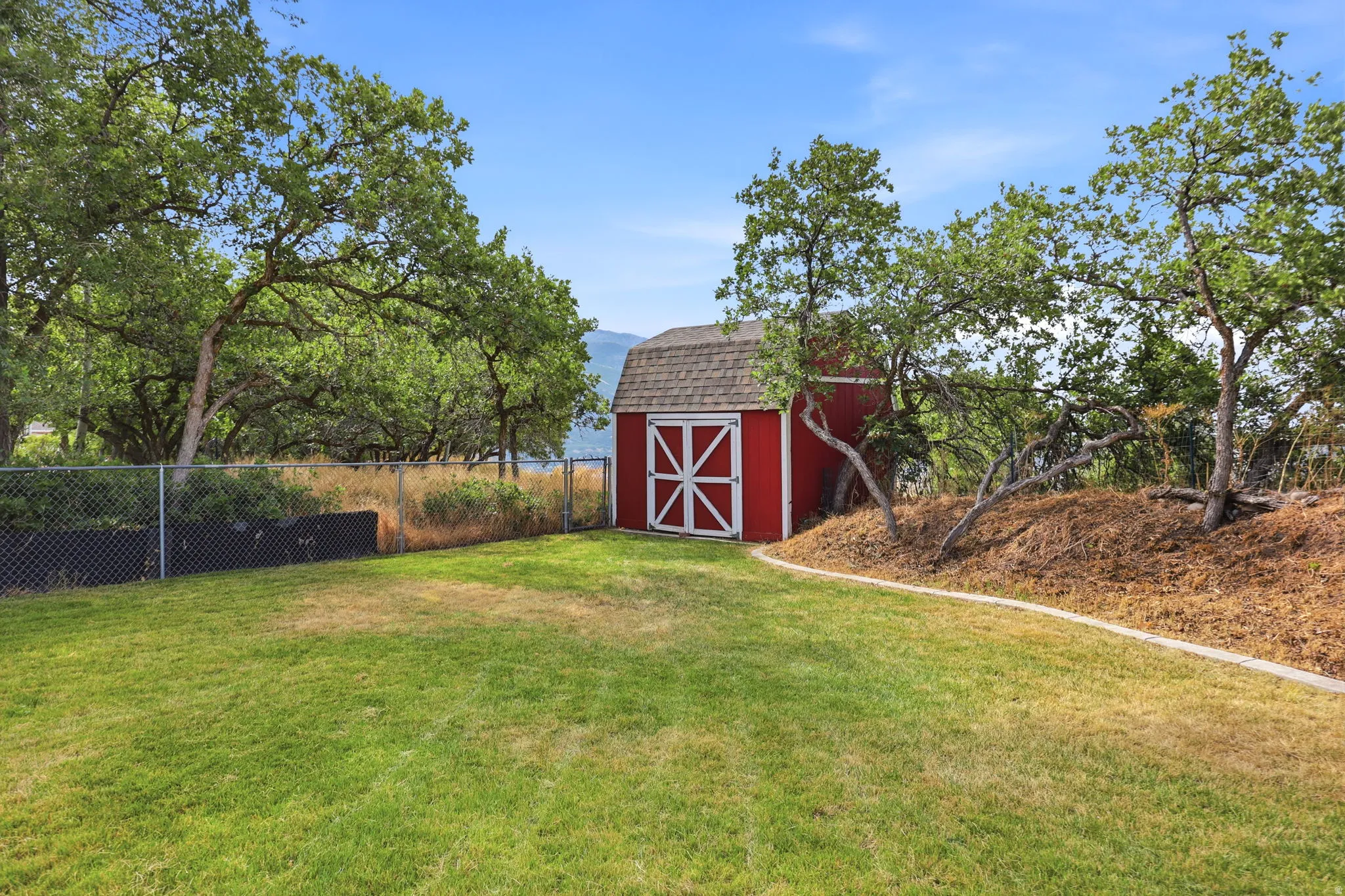 Expansive green lawn with a red storage shed featuring white trim and a shingled roof