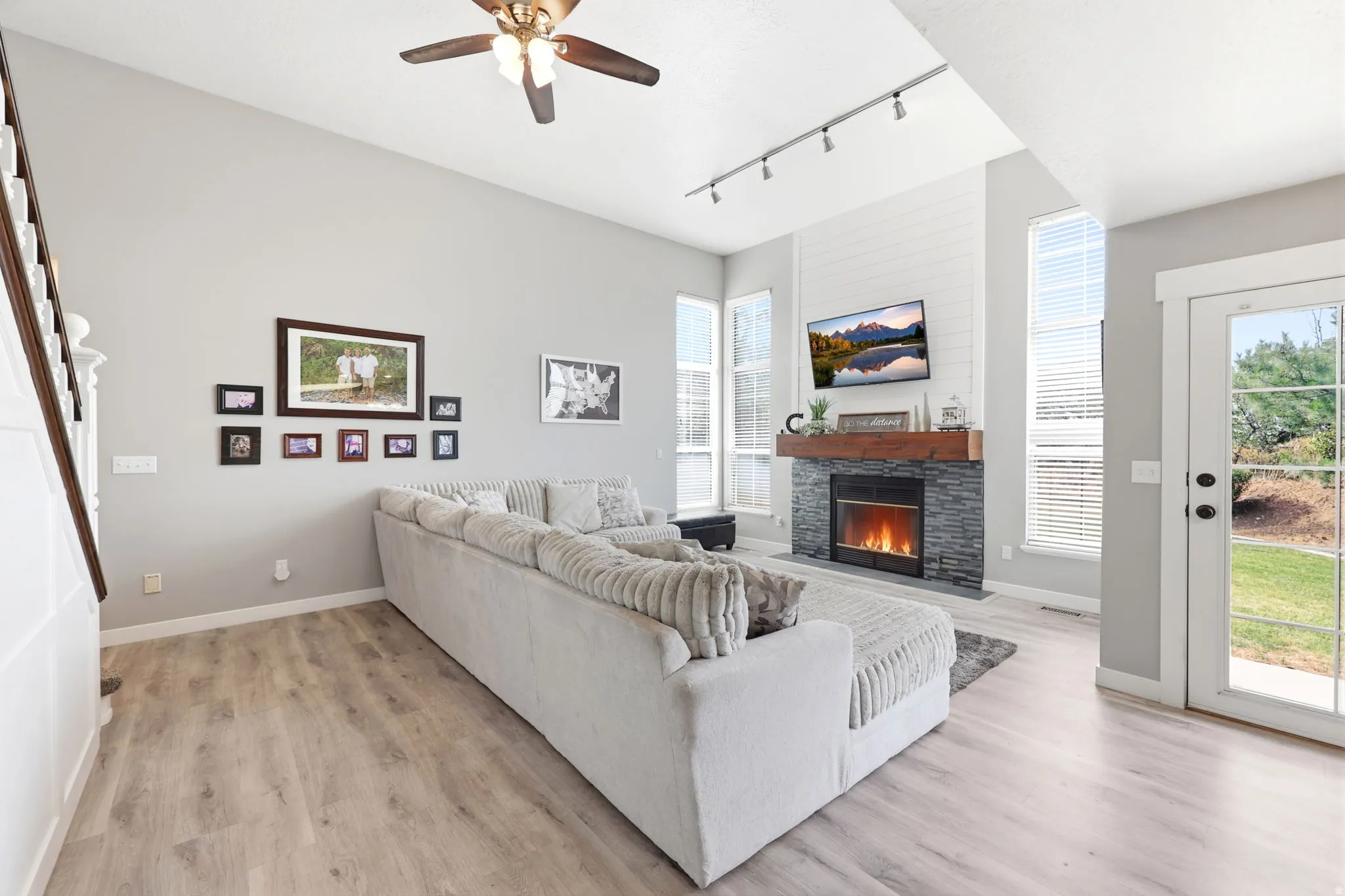 Living area featuring vaulted ceilings, a stone-clad fireplace with a wood mantel, light wood-finish flooring, and a glass-paneled exterior door