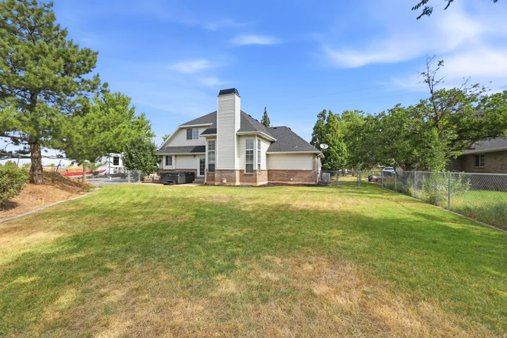 Spacious backyard with a two-story residence featuring a white siding exterior, brick accents, a prominent chimney, and a dark shingled roof