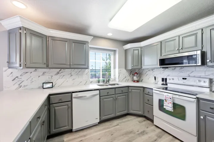 Modern kitchen featuring light gray cabinetry, white countertops, and a white subway tile backsplash with gray veining
