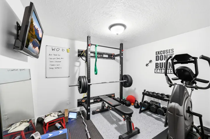 Dedicated fitness space featuring light gray walls, textured white ceiling, and a flush-mount ceiling light