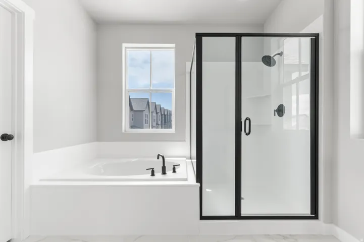 White soaking tub with matte black fixtures, an adjacent black-framed glass shower enclosure, and a window with white trim