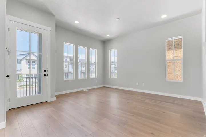 Spacious room featuring wood-finish flooring, recessed lighting, multiple windows, and a glass-paneled door opening to a balcony with a black railing