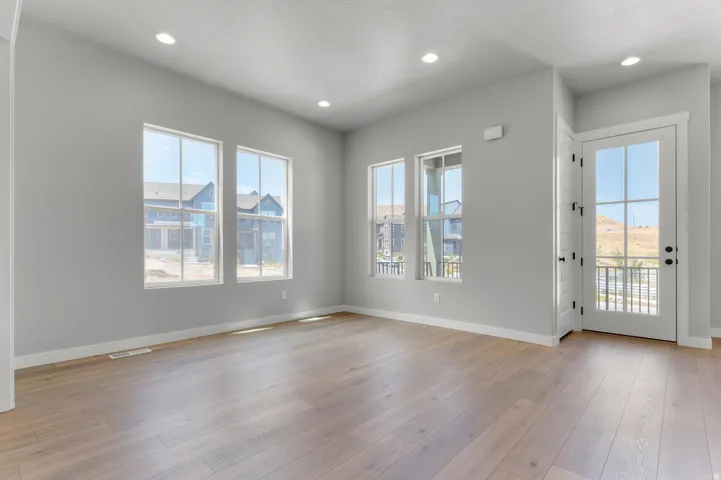 Spacious room featuring light wood-finish flooring, recessed lighting, multiple windows, and a glass-paned door opening to an exterior railing