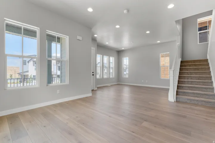 Spacious interior featuring wide-plank wood-finish flooring, recessed lighting, multiple large windows, a carpeted staircase, and neutral wall tones