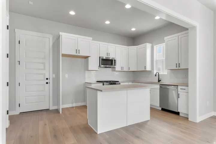Modern kitchen featuring white shaker cabinetry, stainless steel appliances, a center island with countertop, subway tile backsplash, and light wood-finish flooring