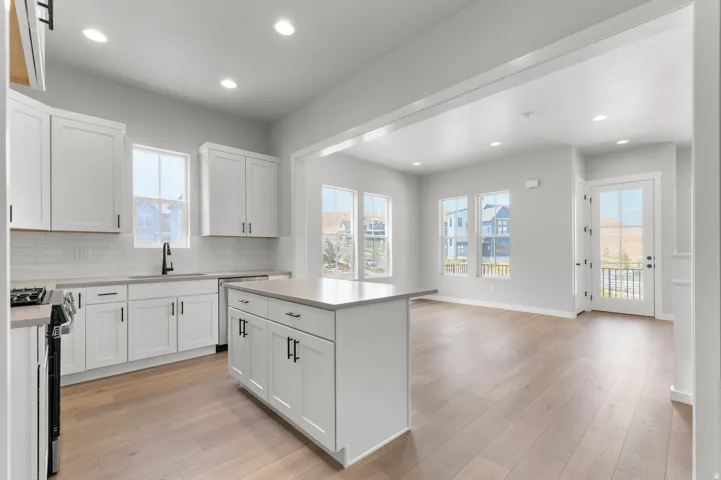 Contemporary kitchen featuring white shaker cabinetry, light-toned wood-finish flooring, a central island with countertop seating, and recessed lighting
