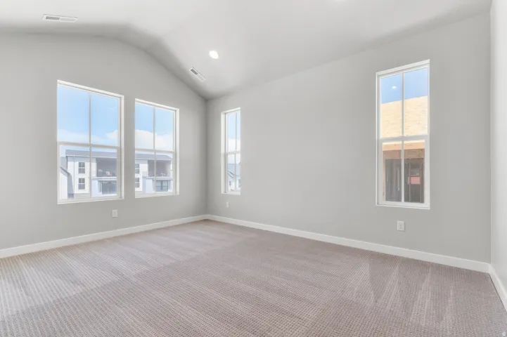 Spacious room featuring a vaulted ceiling with recessed lighting, three tall windows, light gray wall paint, and striped carpet flooring