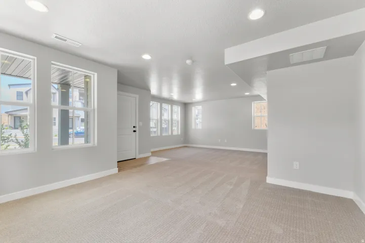 Expansive carpeted area with recessed lighting, multiple windows, and a white paneled door
