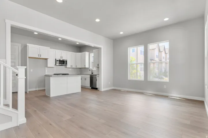Spacious living area featuring light wood-finish flooring, recessed lighting, and multiple windows