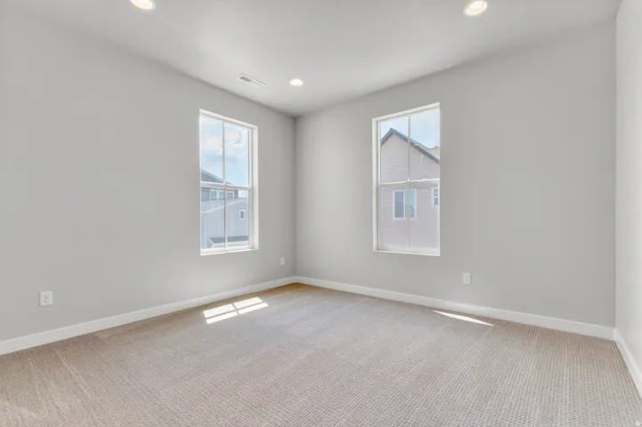Neutral carpeted room featuring two single-hung windows, recessed lighting, white baseboards, and light gray painted walls