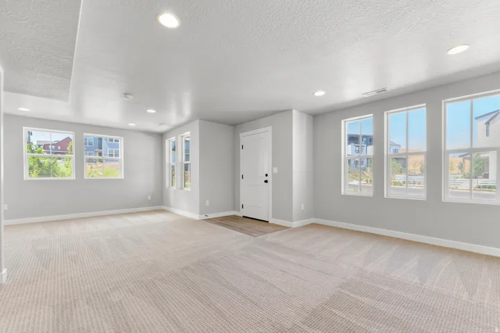 Spacious room featuring neutral carpeting, recessed lighting, multiple windows, light gray wall paint, and white trim