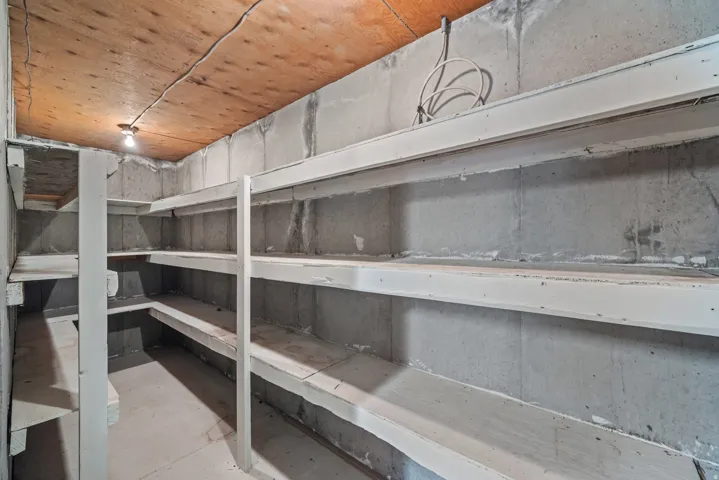 Basement storage room featuring concrete walls, wood-finish ceiling, and built-in shelving units