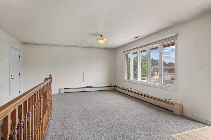 Spacious room featuring multiple large windows, wall-to-wall carpeting, and baseboard heating
