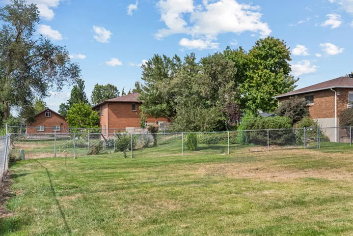 Expansive grassy yard area featuring chain-link fencing and mature perimeter trees