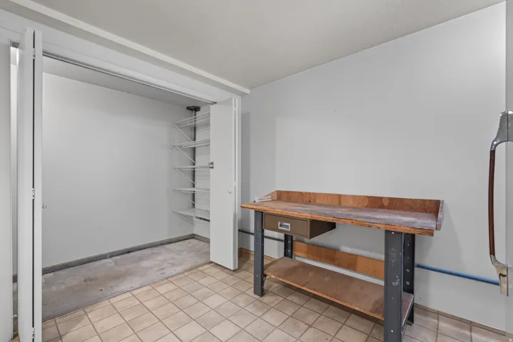 Utility space featuring light-toned tile flooring, white walls, and a built-in workbench with a storage drawer