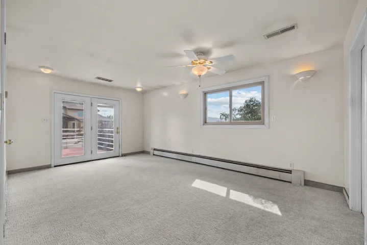 Spacious room featuring light-colored carpeting, white walls, and a ceiling fan with integrated lighting