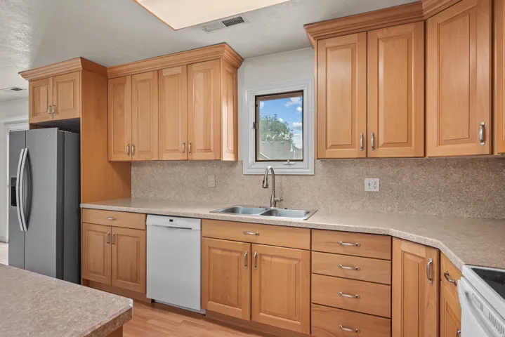 Kitchen featuring natural wood cabinetry, light-toned countertops, double basin stainless steel sink, and wood-finish flooring