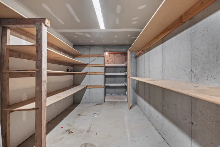 Spacious storage area featuring extensive built-in shelving, concrete walls, concrete flooring, and ceiling-mounted strip lighting