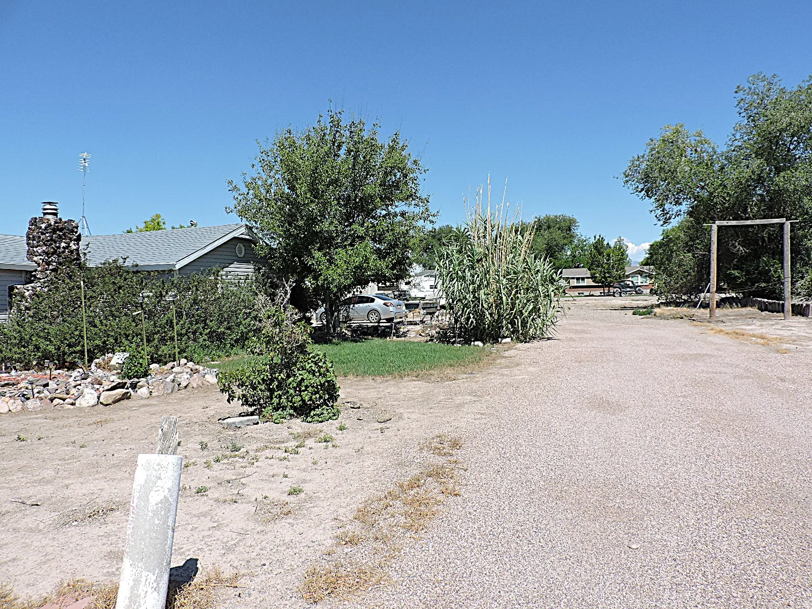 Gravel driveway extending towards a single-story residence with a grey roof and siding