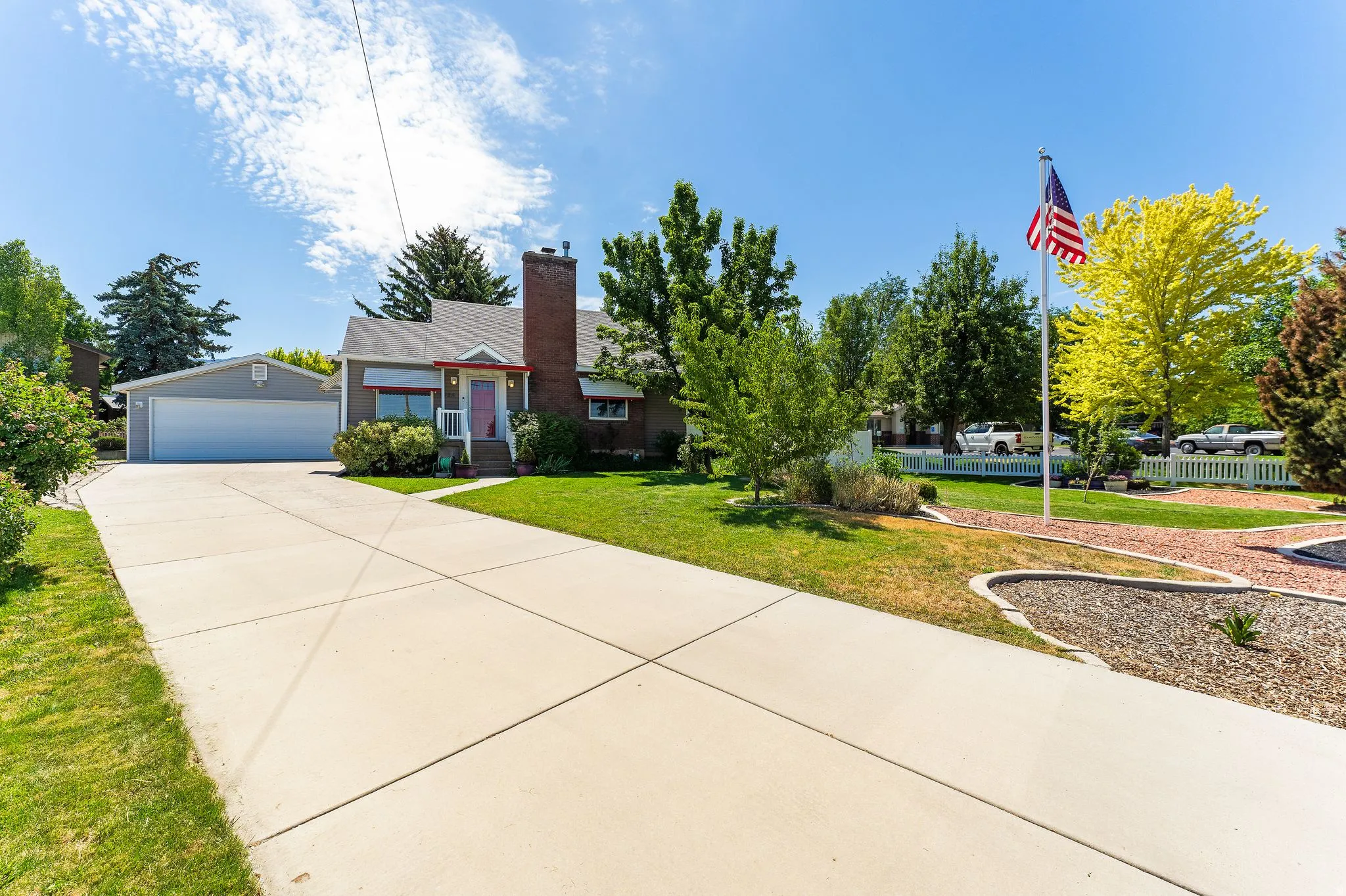 Single-story residence featuring a two-car garage, expansive concrete driveway, and a red brick chimney