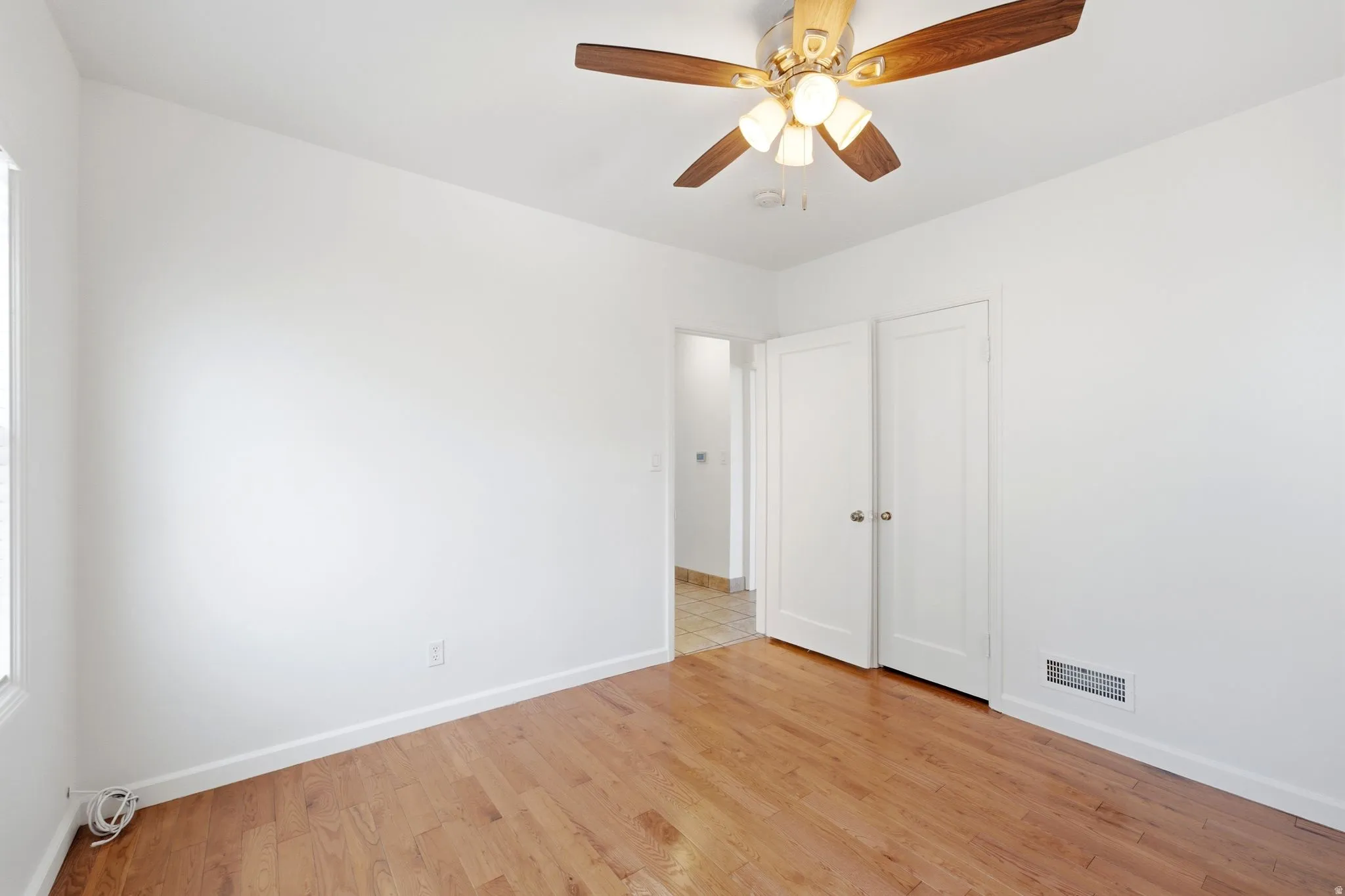 Hardwood flooring throughout featuring white baseboards, a ceiling fan with light fixture, and white bi-fold closet doors with round hardware