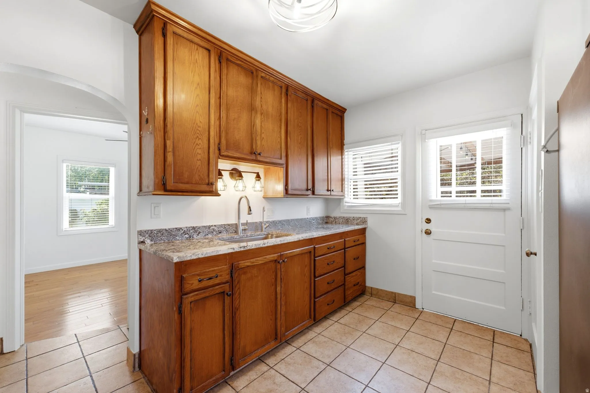 Kitchenette featuring wood cabinetry, undermount sink with a gooseneck faucet, light-toned stone countertop, and tile flooring