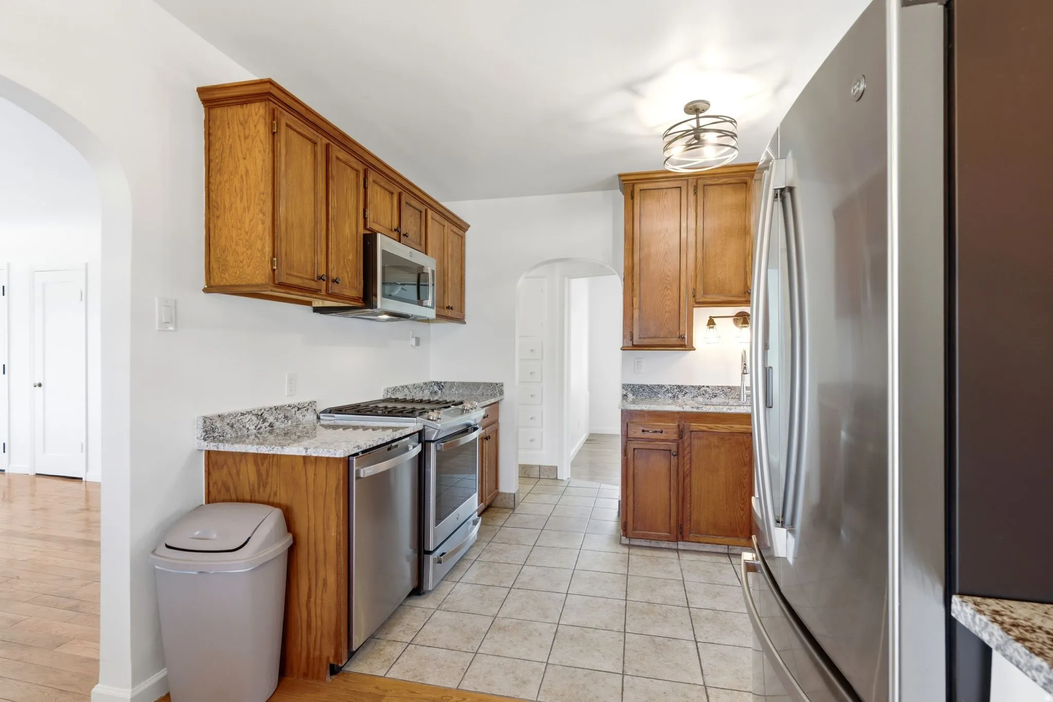 Kitchen featuring wood cabinetry, stainless steel appliances, speckled stone countertops, and tile flooring