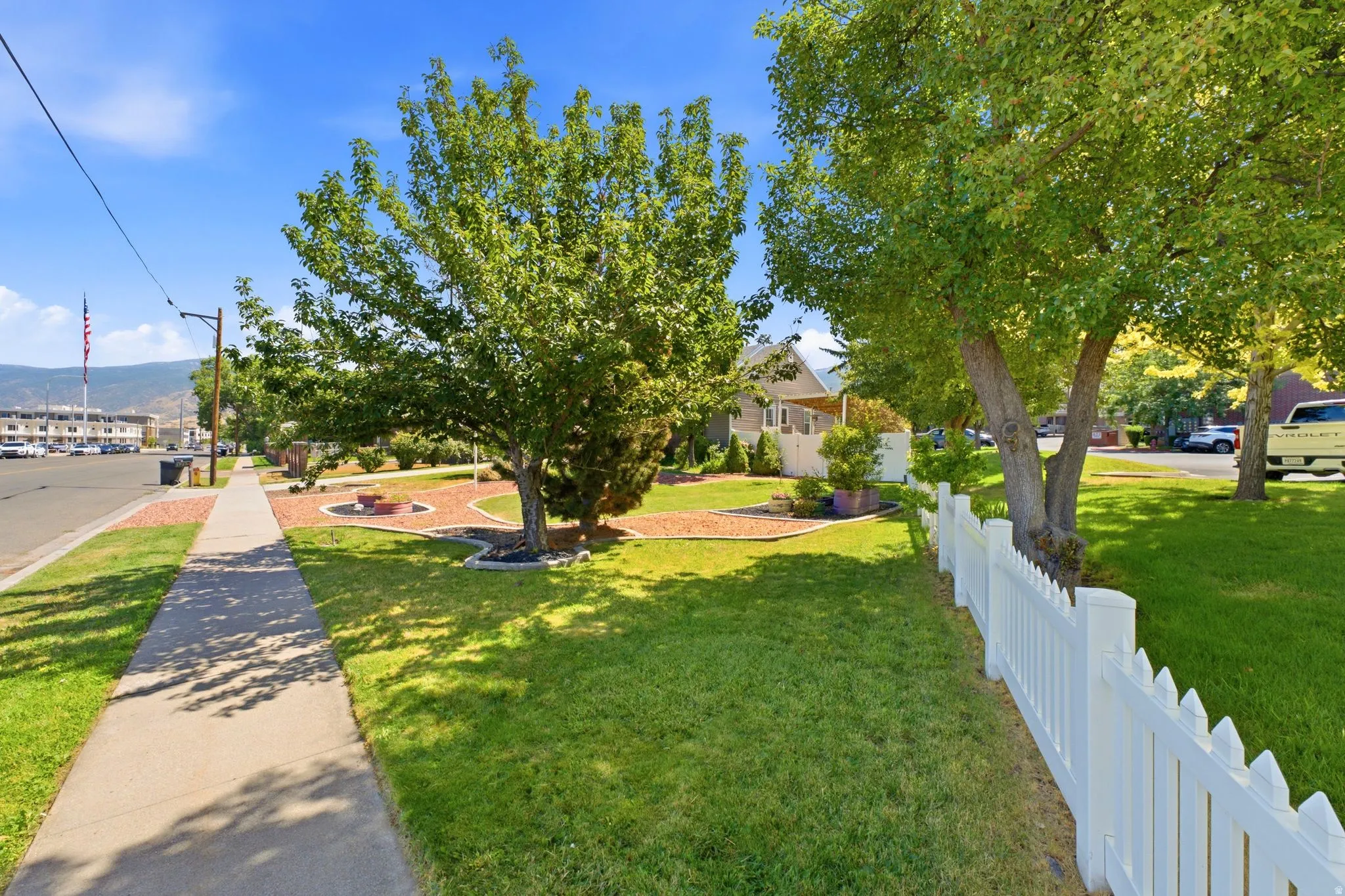 Manicured front yard with mature trees, a white picket fence, and decorative landscaping