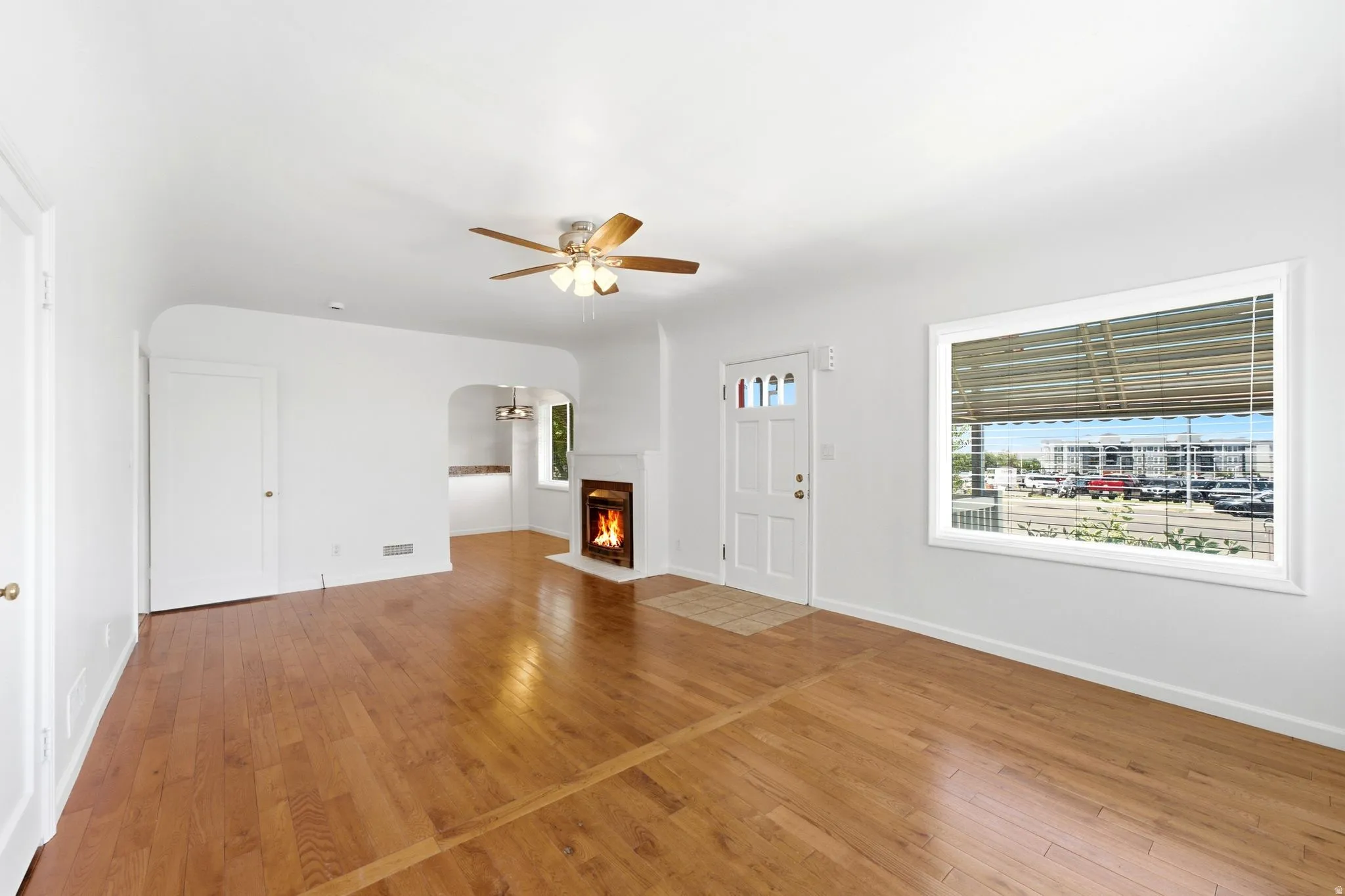 Living area featuring wood-finish flooring, a ceiling fan, a fireplace with a white mantel, and a front entry door with glass inserts