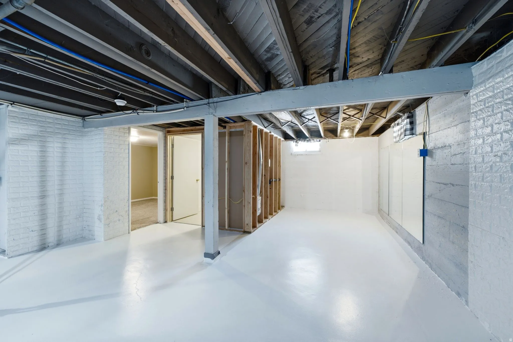 Spacious basement area featuring a bright white floor and painted brick walls