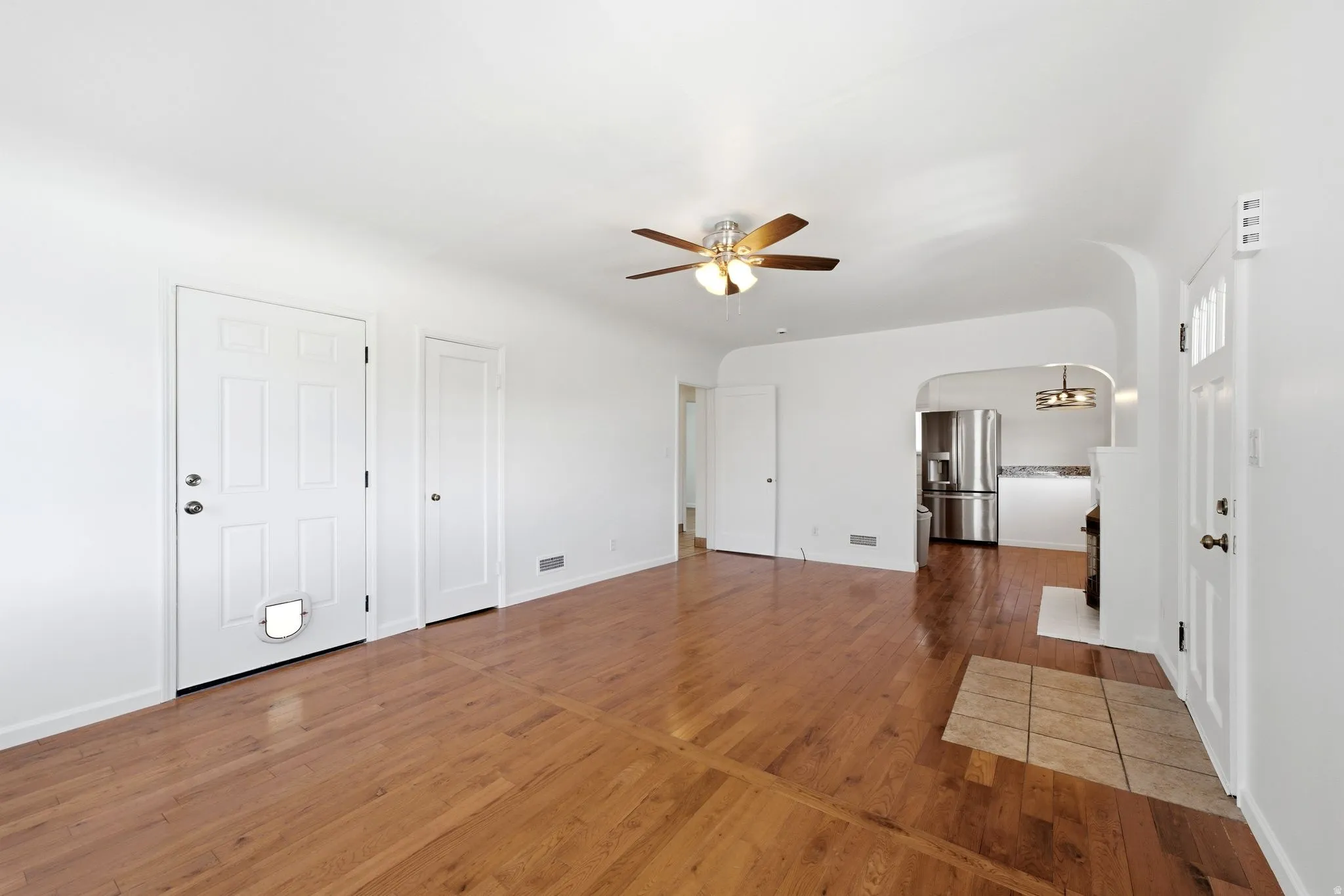 Living area featuring wood-finish flooring, a ceiling fan with integrated lighting, and an arched doorway leading to the kitchen