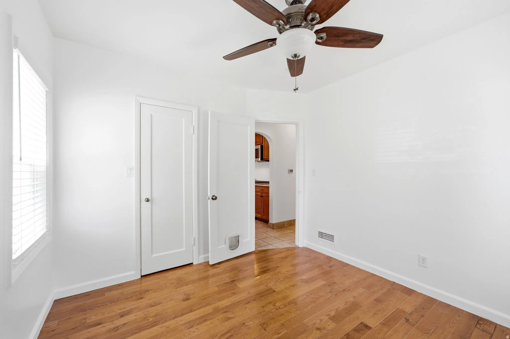 Room featuring wood-finish flooring, a ceiling fan with light fixture, and white window blinds