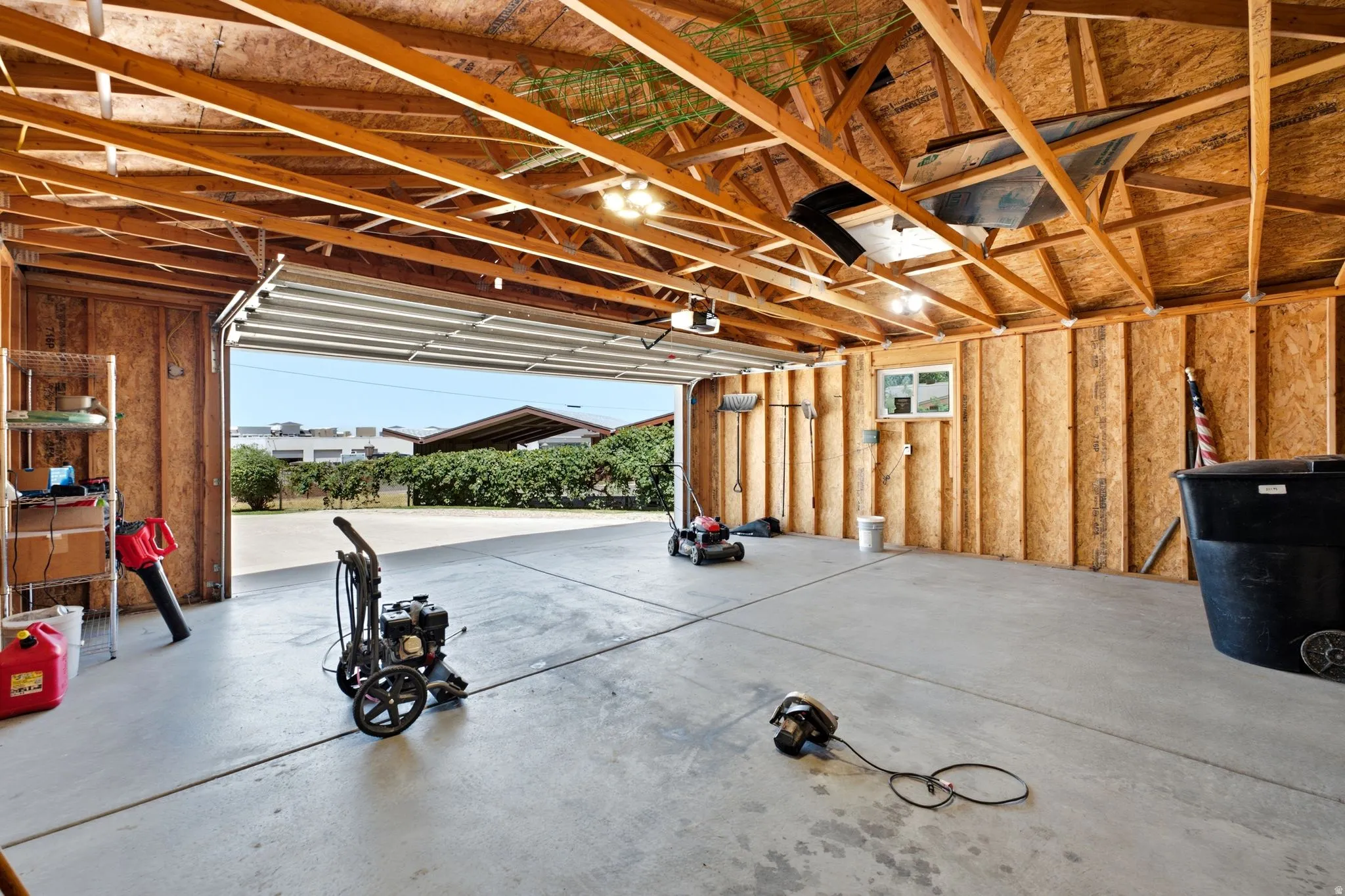 Spacious garage featuring exposed wood beam ceiling, concrete flooring, a single window, and an overhead door