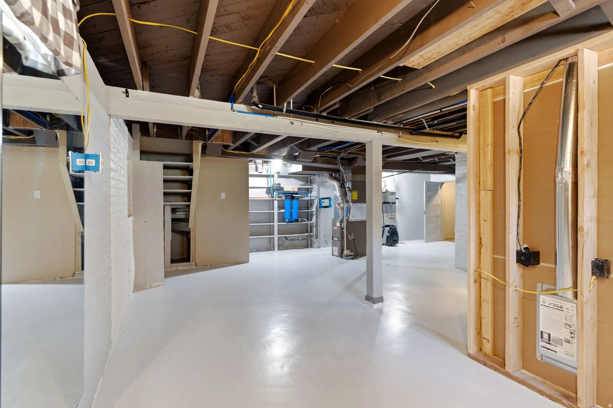 Unfinished lower level featuring exposed ceiling joists, white painted concrete flooring, and a partial wood stud wall framing