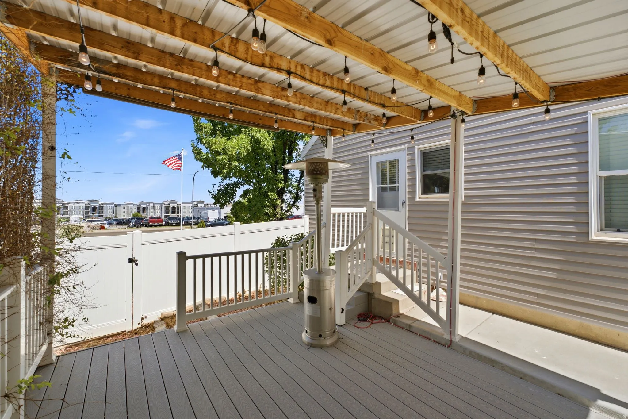 Covered outdoor deck featuring composite decking, white railings, and a wood-beamed ceiling with string lighting