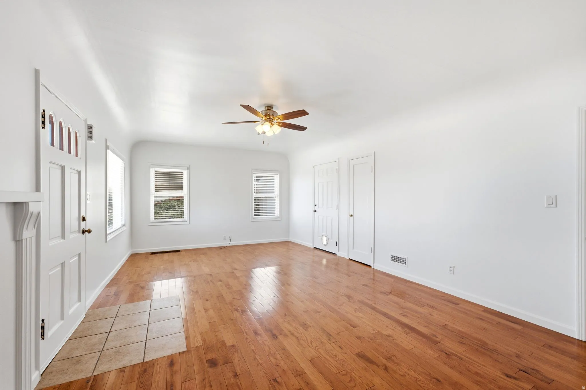 Spacious interior featuring wood-finish flooring, white walls, and a ceiling fan with integrated lighting