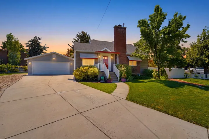 Front exterior featuring a brick chimney, white picket fence, attached two-car garage, concrete driveway, and established landscaping