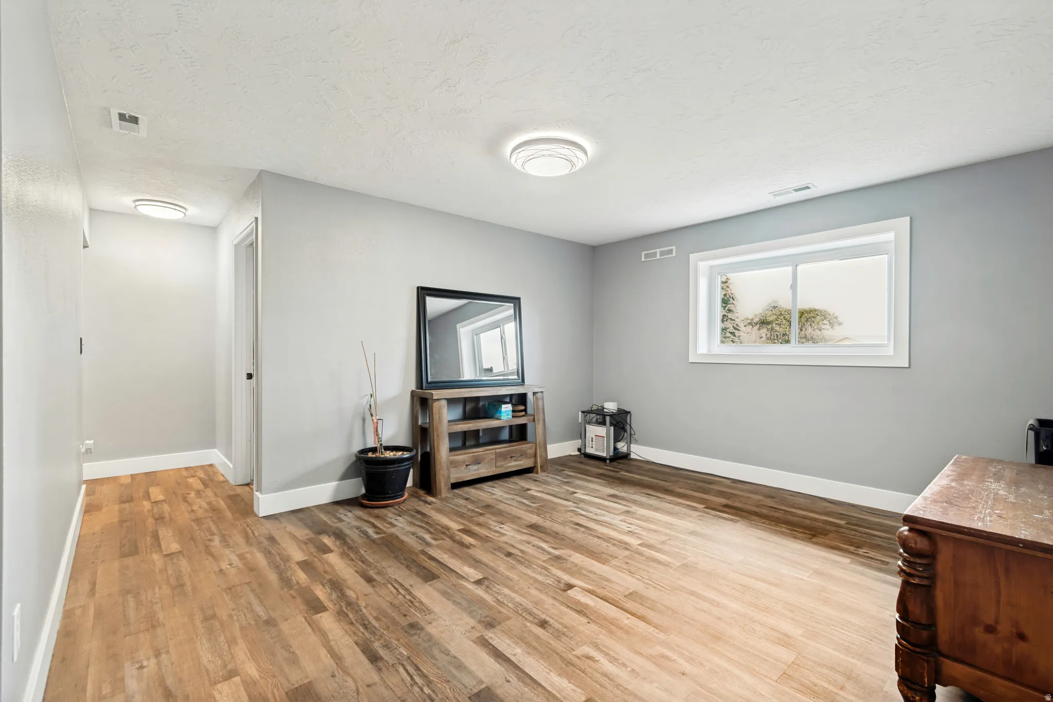 Spacious room with wood-finish flooring, light gray wall paint, white baseboards, and a white ceiling