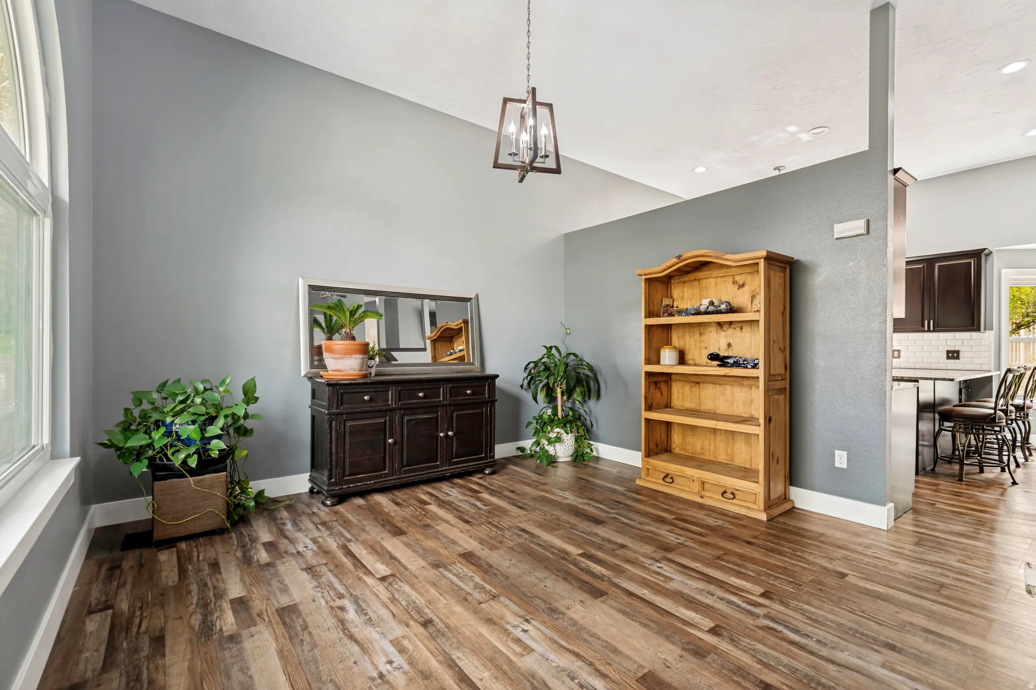 Spacious interior room featuring wood-finish flooring, vaulted ceilings, a large window, and a contemporary hanging light fixture