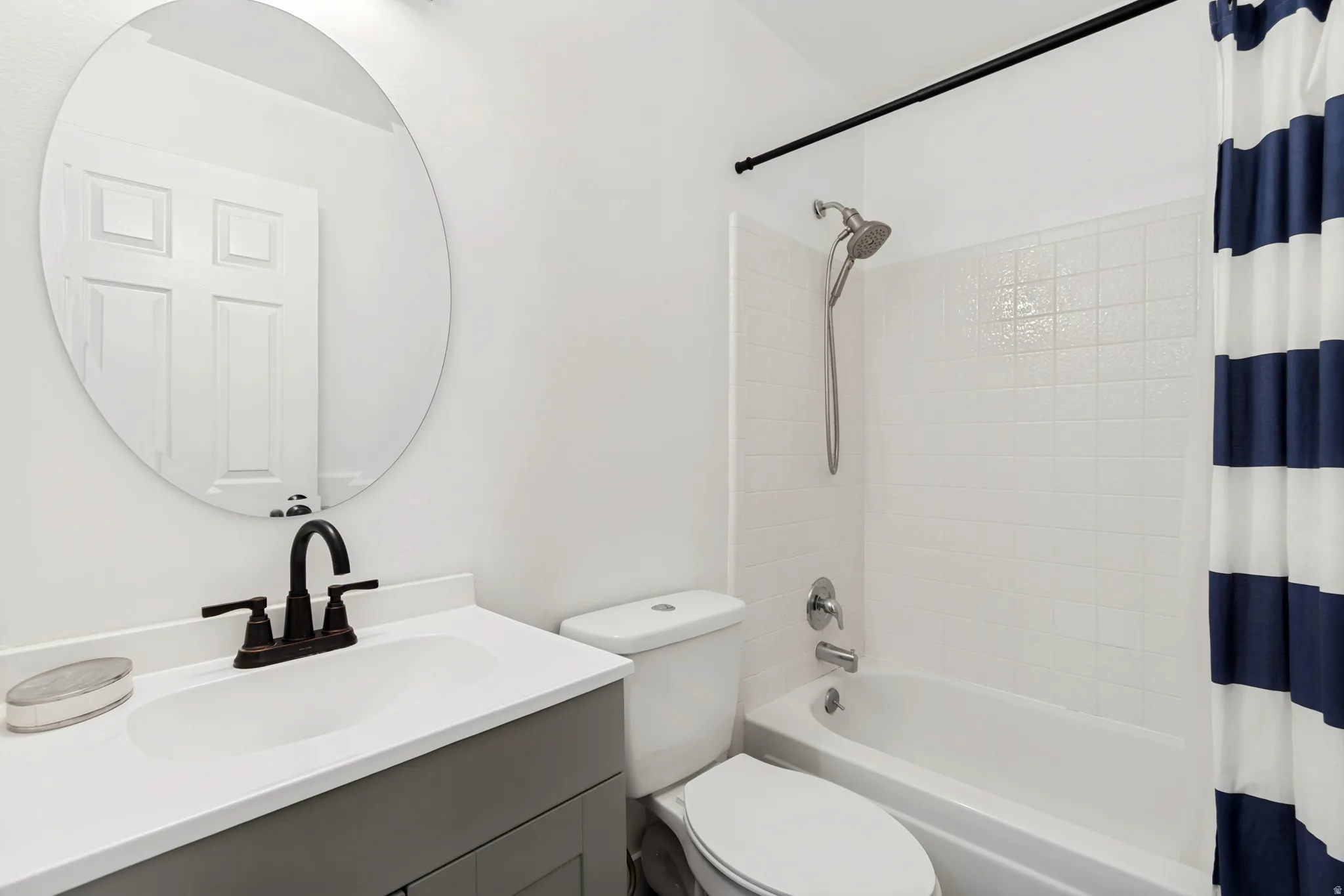 Bathroom featuring a vanity with an integrated sink, dark bronze faucet, and a circular mirror