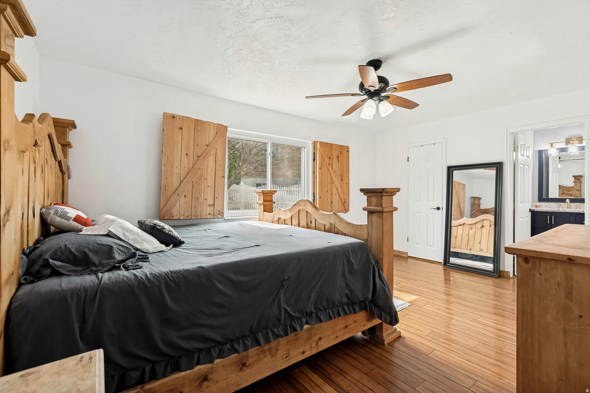 Bright bedroom featuring wood-finish flooring, a ceiling fan with integrated lighting, and natural light from a window with decorative wooden shutters