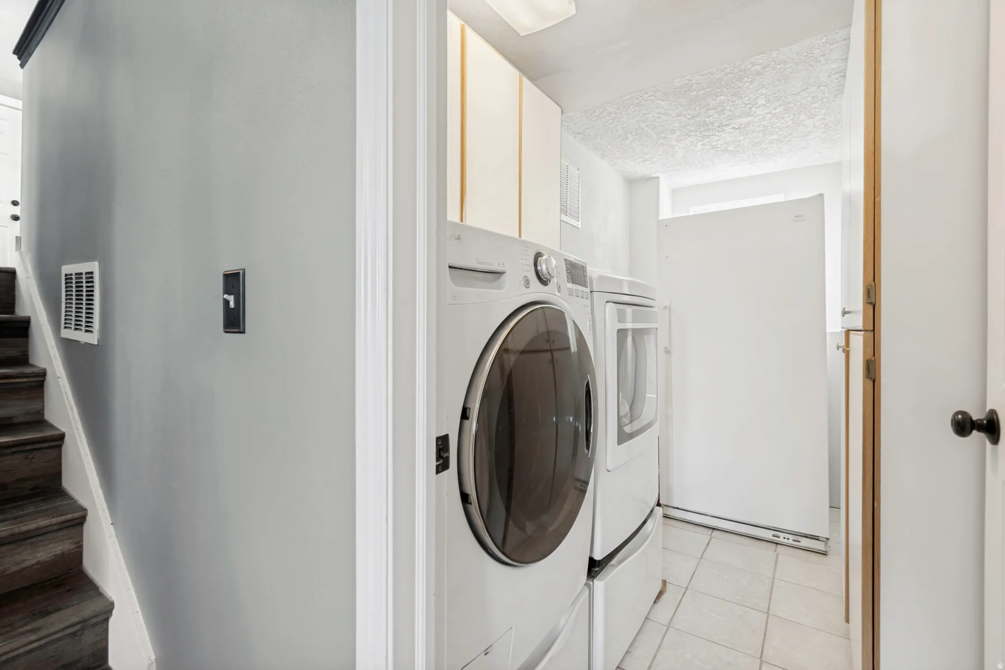 Dedicated laundry area featuring a front-load washer and dryer set, overhead cabinetry, and tiled flooring